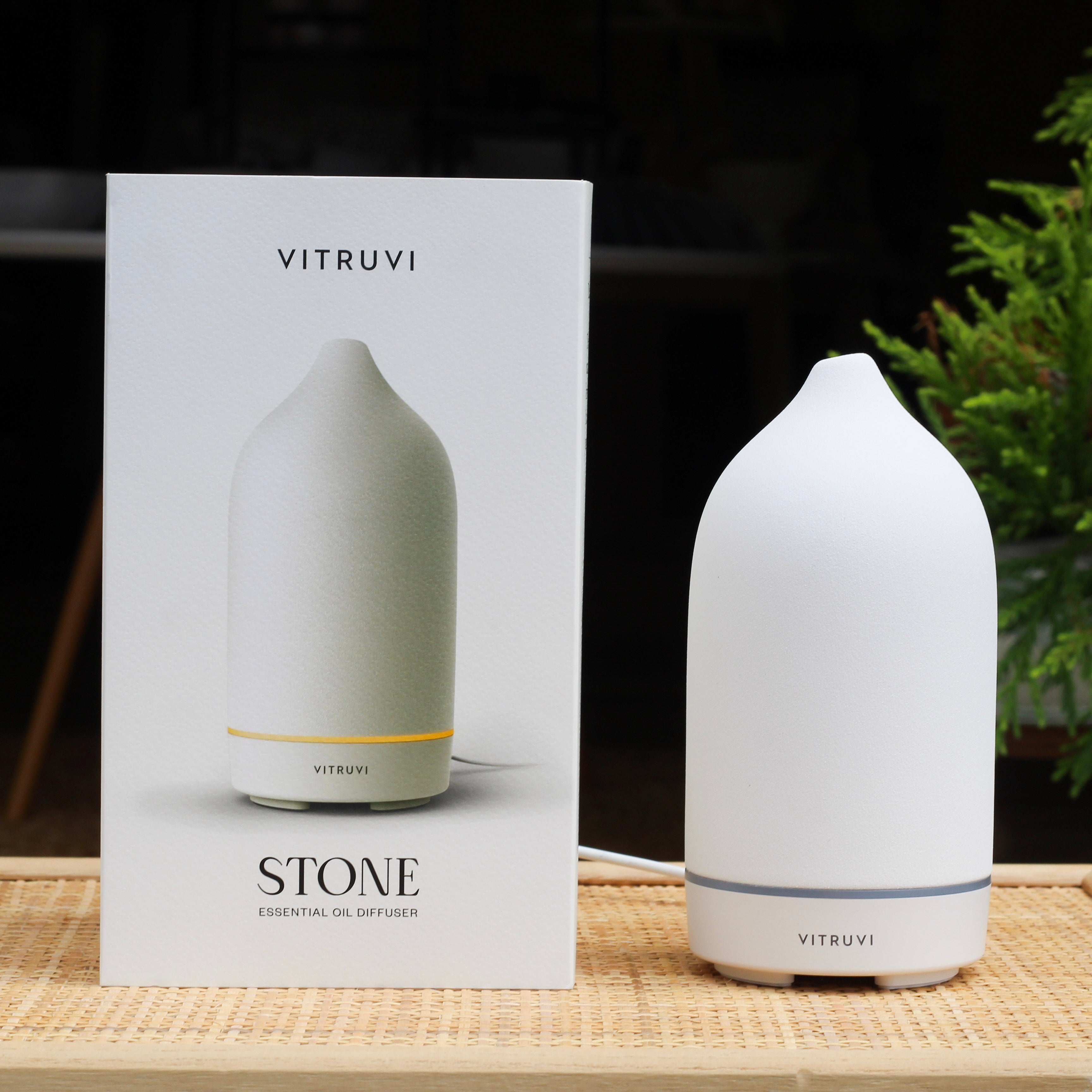 Vitruvi Stone essential oil diffuser next to its packaging on a wooden surface with a blurred background.