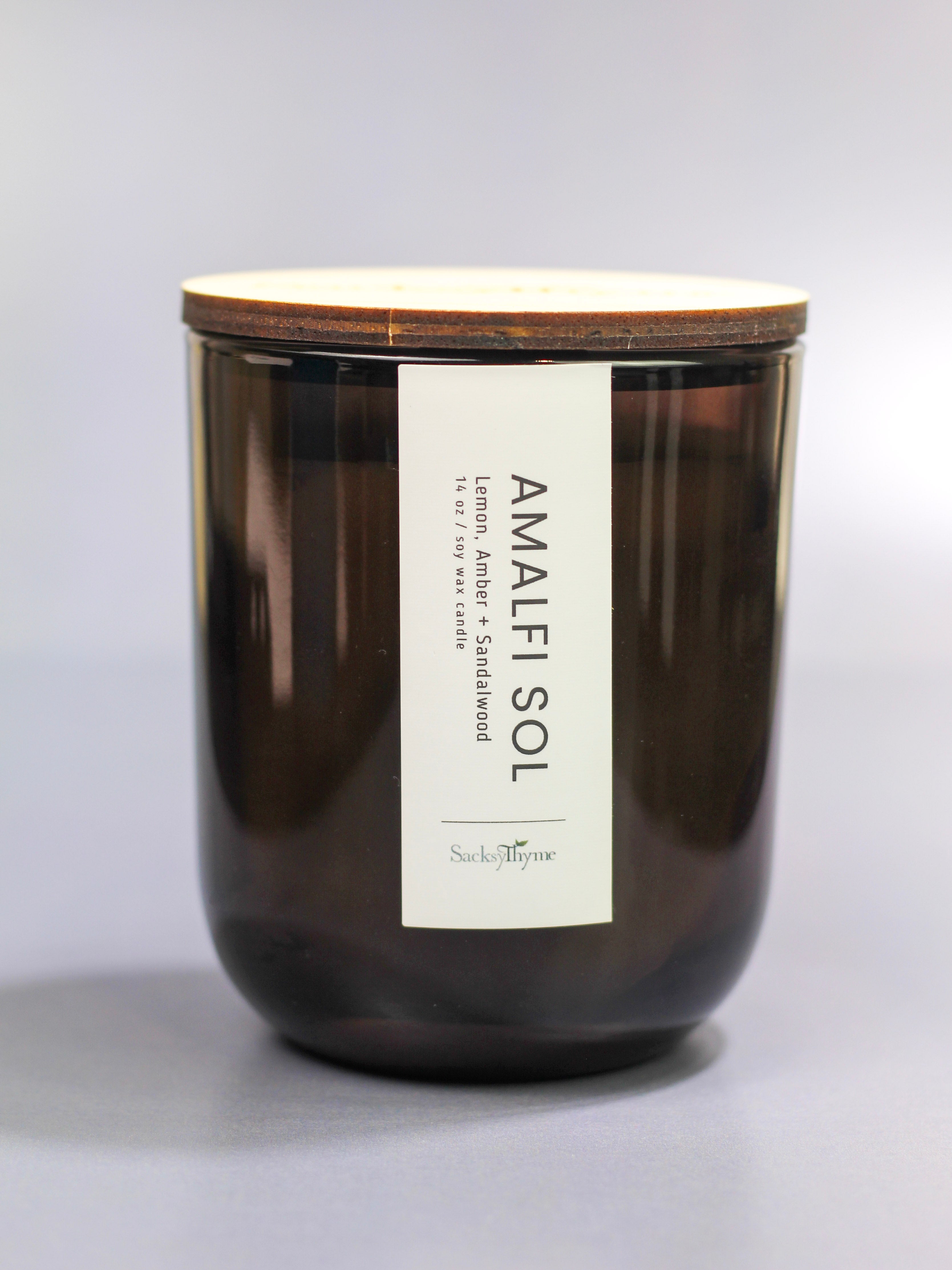 Dark glass candle with wooden lid and 'Amalfi Sol' label on a light gray background