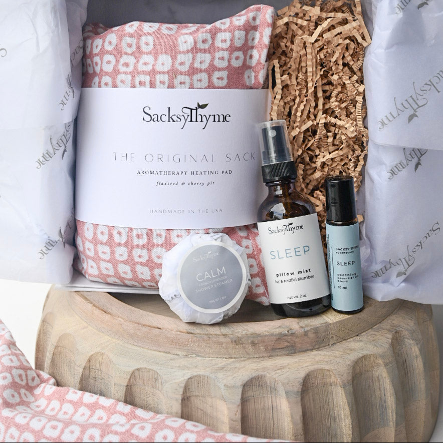 SackThyme product set including a heating pad, diffuser, and bottles on a wooden stand.